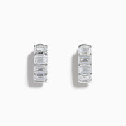 A pair of Lab Grown Emerald Cut Diamond Huggie Earrings in 14K white gold, each featuring three vertically-set rectangular clear stones, is displayed against a plain white background.