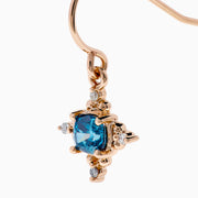 The Bella Bleu 14K Rose Gold Blue and White Diamond Earrings feature round blue gemstones at the center, accented by small white diamonds and gold detailing, beautifully showcased against a white background.