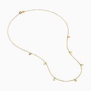 The 14K Yellow Gold Oval Charm Station Necklace features small, evenly spaced oval-shaped charms that hang gracefully along the lower half of a delicate yellow gold chain.