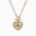 The 14K Yellow Gold Fresh Water Pearl Sapphire and Diamond Necklace features beaded pearls, a toggle clasp, and a heart-shaped gold pendant with an eye design set with diamonds and a central sapphire.