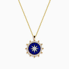 The Seaside 14K Yellow Gold Lapis and Diamond Compass Pendant features a gold chain and round lapis blue pendant with a white starburst design, accented by small gold beads, evoking a compass style. Shown on a plain white background.