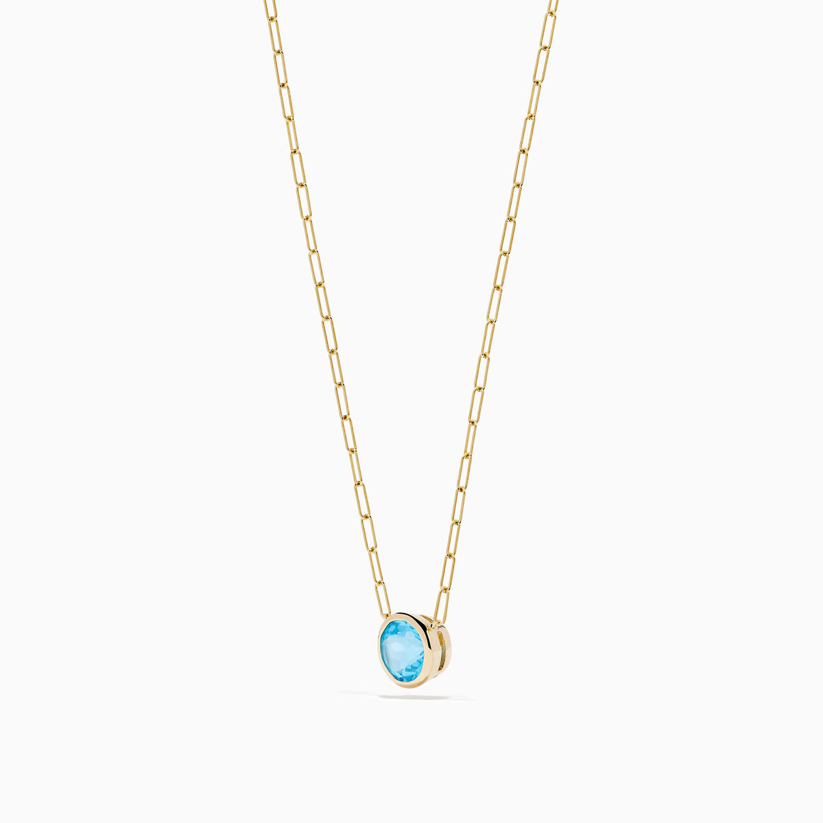 The 14K Yellow Gold Blue Topaz Bezel Paperclip Chain Pendant features a single round blue topaz gemstone on a gold paperclip chain, beautifully displayed against a white background.