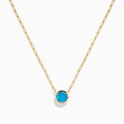 The 14K Yellow Gold Blue Topaz Bezel Paperclip Chain Pendant features a single round blue topaz gemstone on a gold paperclip chain, beautifully displayed against a white background.