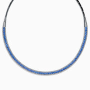 The 14K White Gold Tanzanite and Diamond Collar Necklace showcases a row of vivid blue tanzanites edged with sparkling diamonds on a sleek curved band, elegantly displayed against a white background.