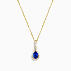 The Nahla 14K Yellow Gold Tanzanite Pendant features a teardrop blue tanzanite surrounded by diamonds and a diamond-accented bail, gleaming at the center of this elegant necklace.