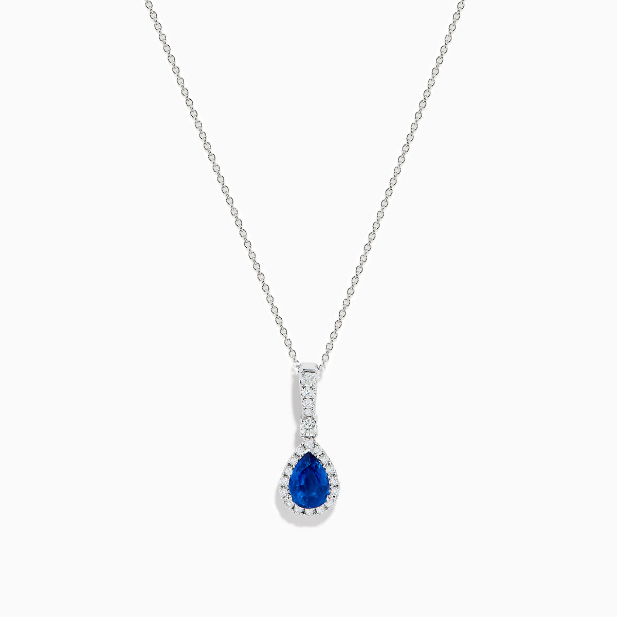 The 14K White Gold Pear Shape Blue Sapphire and Diamond Pendant features a teardrop blue sapphire framed by small clear stones and accented with diamonds set above the main gem.