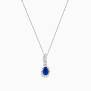 The 14K White Gold Pear Shape Blue Sapphire and Diamond Pendant features a teardrop blue sapphire framed by small clear stones and accented with diamonds set above the main gem.