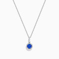 The 14K White Gold Tanzanite and Diamond Halo Pendant showcases a round tanzanite encircled by sparkling diamonds, set on a delicate chain, against a white background.