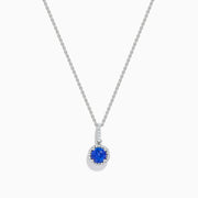 The 14K White Gold Tanzanite and Diamond Halo Pendant showcases a round tanzanite encircled by sparkling diamonds, set on a delicate chain, against a white background.