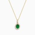 The 14K Yellow Gold Emerald and Diamond Pendant features an oval emerald surrounded by diamonds, suspended from a delicate gold chain and displayed against a white background.