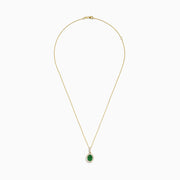 The 14K Yellow Gold Emerald and Diamond Pendant features an oval emerald surrounded by diamonds, suspended from a delicate gold chain and displayed against a white background.