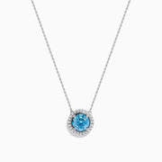 The Lab Grown Blue and White Diamond Halo Necklace in 14K White Gold features a round blue gemstone pendant encircled by sparkling lab grown diamonds, shown against a white background.