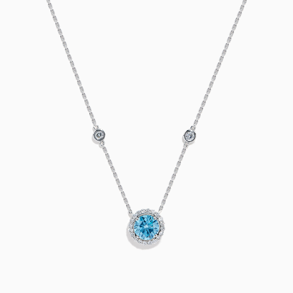 The Lab Grown Blue and White Diamond Halo Necklace in 14K White Gold features a round blue gemstone pendant surrounded by lab grown diamonds, plus two small clear stones set along the chain.