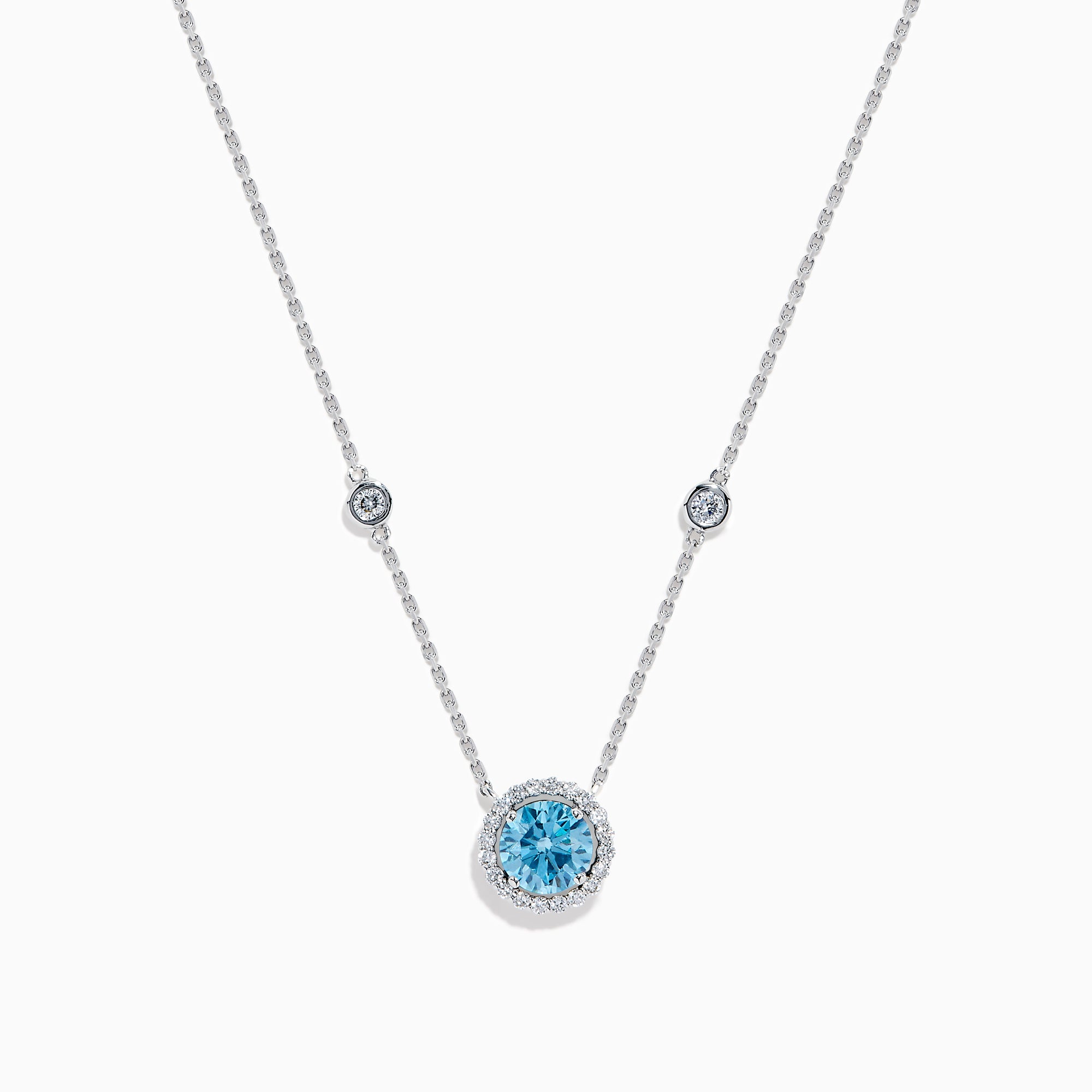 The Lab Grown Blue and White Diamond Halo Necklace in 14K White Gold features a round blue gemstone pendant surrounded by lab grown diamonds, plus two small clear stones set along the chain.
