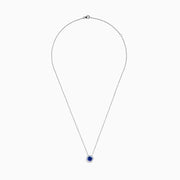 The Nahla 14K White Gold Tanzanite and Diamond Halo Necklace features a round blue tanzanite pendant encircled by sparkling diamonds on a delicate silver chain, creating an elegant look against a plain white background.
