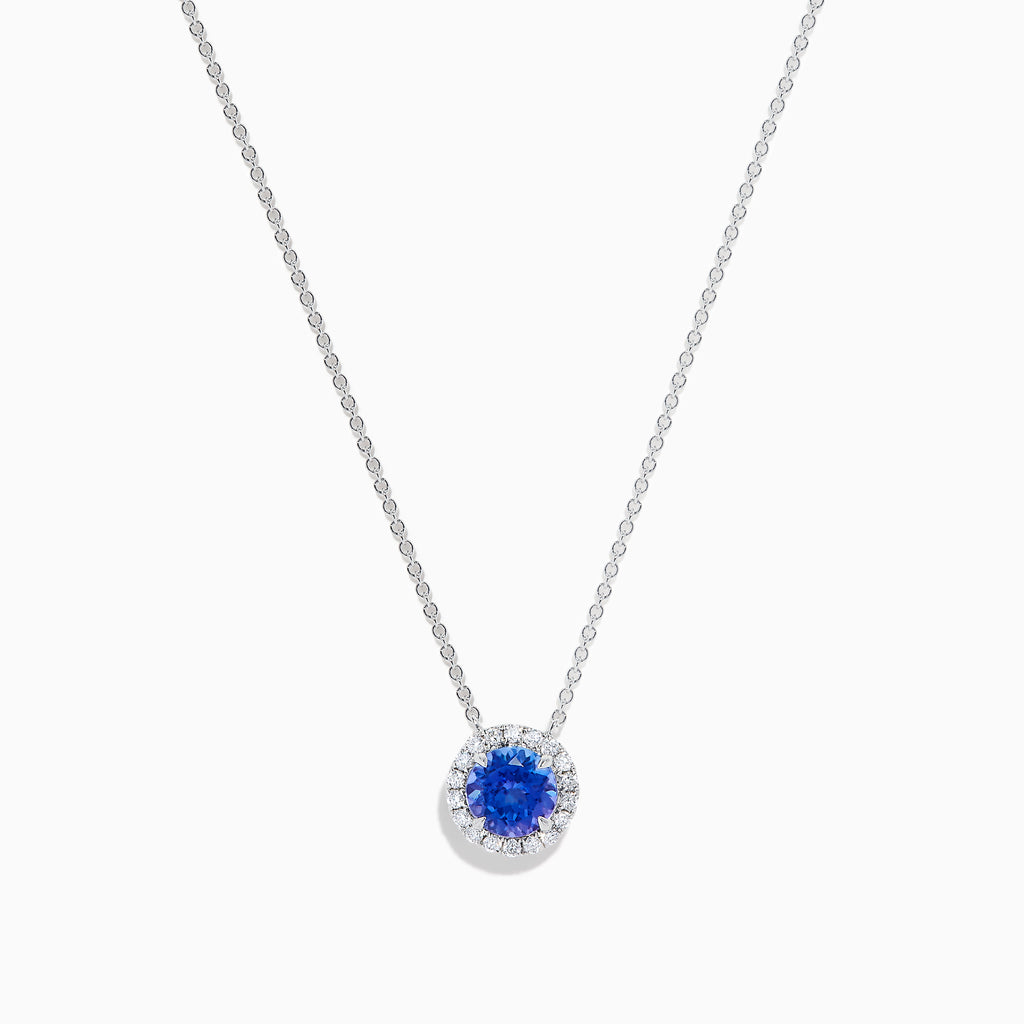 The Nahla 14K White Gold Tanzanite and Diamond Halo Necklace features a round blue tanzanite pendant encircled by sparkling diamonds on a delicate silver chain, creating an elegant look against a plain white background.