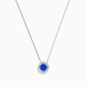 The Nahla 14K White Gold Tanzanite and Diamond Halo Necklace features a round blue tanzanite pendant encircled by sparkling diamonds on a delicate silver chain, creating an elegant look against a plain white background.