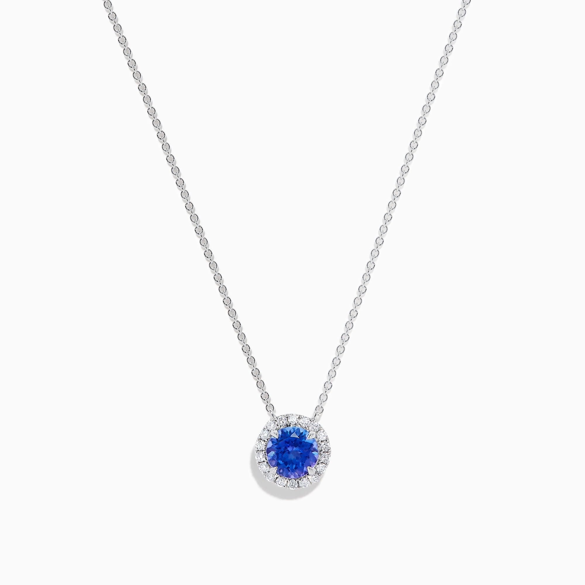 The Nahla 14K White Gold Tanzanite and Diamond Halo Necklace features a round blue tanzanite pendant encircled by sparkling diamonds on a delicate silver chain, creating an elegant look against a plain white background.