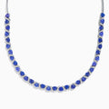 The Nahla Siri 14K White Gold Trillion Cut Tanzanite and Diamond Necklace features alternating deep blue tanzanites and small diamonds set along a 14K white gold chain, elegantly displayed against a white background.