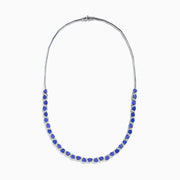 The Nahla Siri 14K White Gold Trillion Cut Tanzanite and Diamond Necklace features alternating deep blue tanzanites and small diamonds set along a 14K white gold chain, elegantly displayed against a white background.