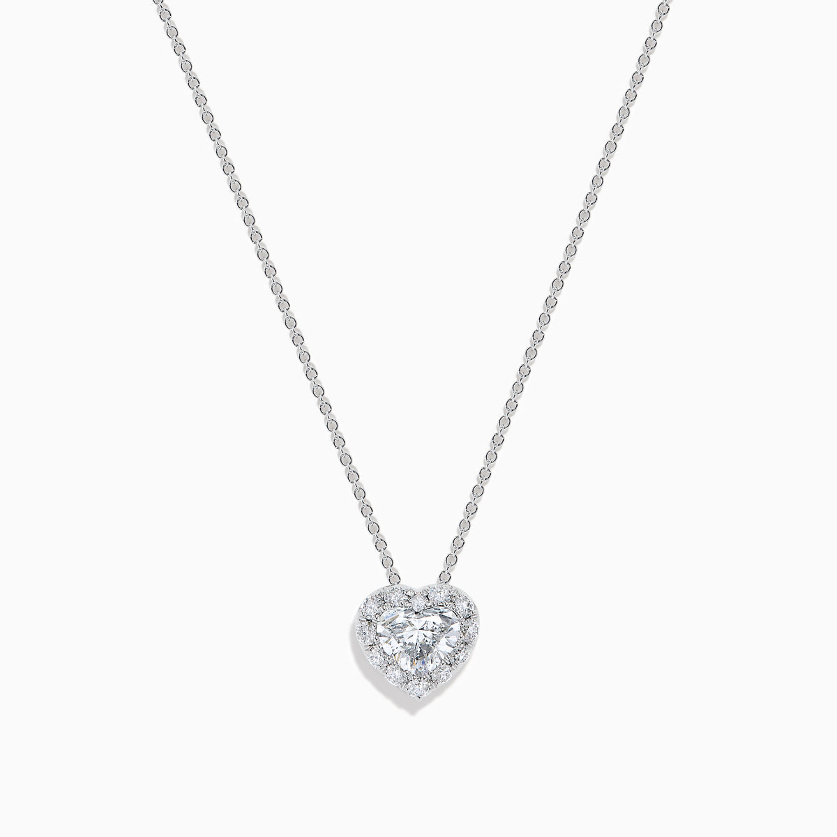 The Lab Grown Heart and Round Diamond Halo Pendant in 14K White Gold features a sparkling heart-shaped lab grown diamond with a halo of smaller diamonds on a delicate silver chain, shown against a plain white background.
