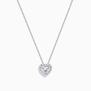 The Lab Grown Heart and Round Diamond Halo Pendant in 14K White Gold features a sparkling heart-shaped lab grown diamond with a halo of smaller diamonds on a delicate silver chain, shown against a plain white background.