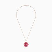 The Ruby Royale 14K Rose Gold Ruby and Diamond Flower Pendant features a round floral design with rubies and diamond accents at the center and edges.
