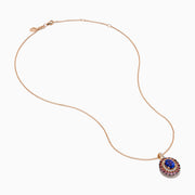 The 14K Rose Gold Pink Sapphire, Tanzanite, and Diamond Double Halo Pendant features an oval-shaped blue gemstone surrounded by pink sapphires, tanzanite, and diamonds on a delicate 14K rose gold chain attached at the top.