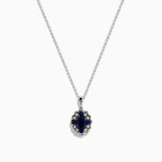 A 14K white gold Sapphire and Diamond Vintage Halo Pendant, featuring a large oval blue sapphire surrounded by smaller diamonds in a floral pattern, is displayed on a white background.