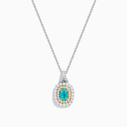 The 18K Two Tone Gold Paraiba and Diamond Double Halo Pendant showcases an oval Paraiba centerpiece, surrounded by a halo of yellow stones and a second halo of sparkling diamonds.