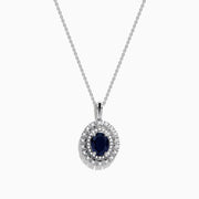 The Royal Bleu 14K White Gold Sapphire & Diamond Halo Pendant features a vibrant sapphire framed by two rows of sparkling white diamonds, all set in a chain necklace against a plain white background.