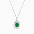 A 14K white gold pendant featuring an oval emerald, surrounded by a double halo of sparkling diamonds.