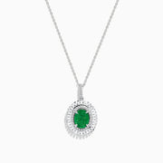 A 14K white gold pendant featuring an oval emerald, surrounded by a double halo of sparkling diamonds.