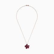The Ruby Royale 14K Rose Gold Ruby and Diamond Flower Pendant showcases a rose gold chain with a flower-shaped design, featuring vibrant rubies, black stones, and sparkling diamonds at the center and petal edges.
