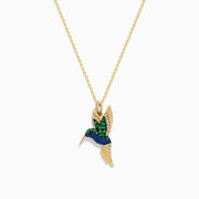 The Safari 14k Yellow Gold Emerald and Sapphire Humming Bird Pendant features a hummingbird-shaped design with emerald and sapphire accents, shown against a white background.