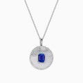 The 14K White Gold Tanzanite and Diamond Fluted Circle Pendant features a round diamond-accented design with a radiant motif and a central emerald-cut blue tanzanite stone.