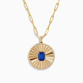 The Nahla Siri 14K Yellow Gold Tanzanite and Diamond Pendant features a round sunburst design with a central blue tanzanite gemstone, accented by diamonds, on an elongated link gold chain.