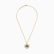 The Nahla Siri 14K Yellow Gold Tanzanite and Diamond Pendant features a round sunburst design with a central blue tanzanite gemstone, accented by diamonds, on an elongated link gold chain.
