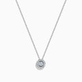 The 14K White Gold Diamond Bezel Halo Pendant features a delicate white gold chain with a round, flower-like diamond pendant, showcasing a central diamond surrounded by a halo of smaller diamonds.