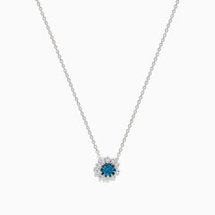 The Bella Bleu 14K White Gold Pendant showcases a round blue and white diamond centerpiece, accented by a halo of 0.60 TCW diamonds, elegantly presented on a white background.