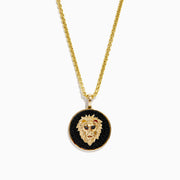The Mens 14K Yellow Gold Black Diamond Lion Head Pendant features a detailed lion head on a black textured background, red eyes, and hangs from a shiny medium-thick chain for an impressive look.