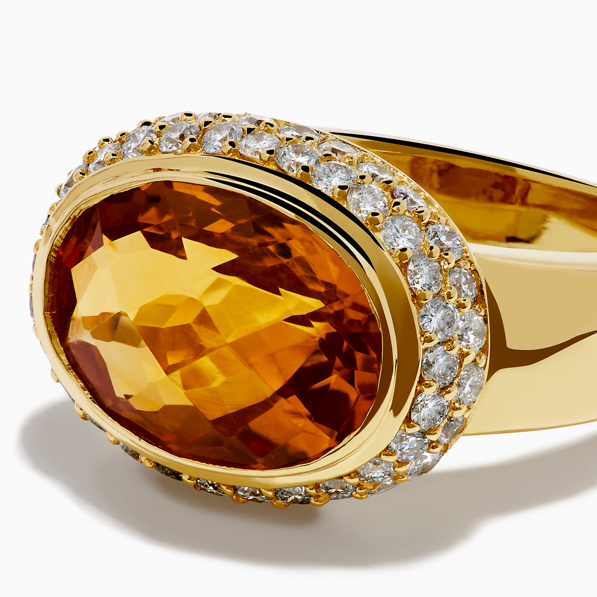 An 18K yellow gold ring featuring an east-west set oval citrine centerpiece, accented by a bezel halo of sparkling diamonds.