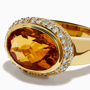 An 18K yellow gold ring featuring an east-west set oval citrine centerpiece, accented by a bezel halo of sparkling diamonds.