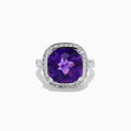 The 18K White Gold Amethyst and Diamond Cushion Halo Cocktail Ring features a striking cushion-cut amethyst center, a sparkling diamond halo, and clear stones on the band, elegantly displayed against a white background.