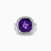The 18K White Gold Amethyst and Diamond Cushion Halo Cocktail Ring features a striking cushion-cut amethyst center, a sparkling diamond halo, and clear stones on the band, elegantly displayed against a white background.