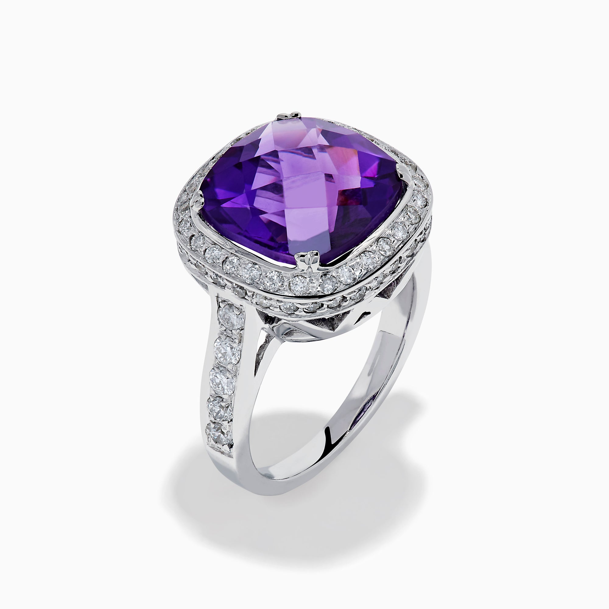 The 18K White Gold Amethyst and Diamond Cushion Halo Cocktail Ring features a striking cushion-cut amethyst center, a sparkling diamond halo, and clear stones on the band, elegantly displayed against a white background.