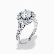 The Star Lab Grown Diamond Fleur Ring in 18K White Gold showcases a large round center lab diamond, with a sparkling halo of smaller diamonds and extra diamonds set along the band.