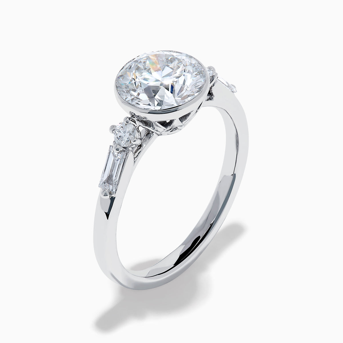 The Star Lab Grown Diamond Moderne Ring in 18K White Gold showcases a large round center diamond with two smaller diamonds on each side, set on a sleek, polished band against a white background.