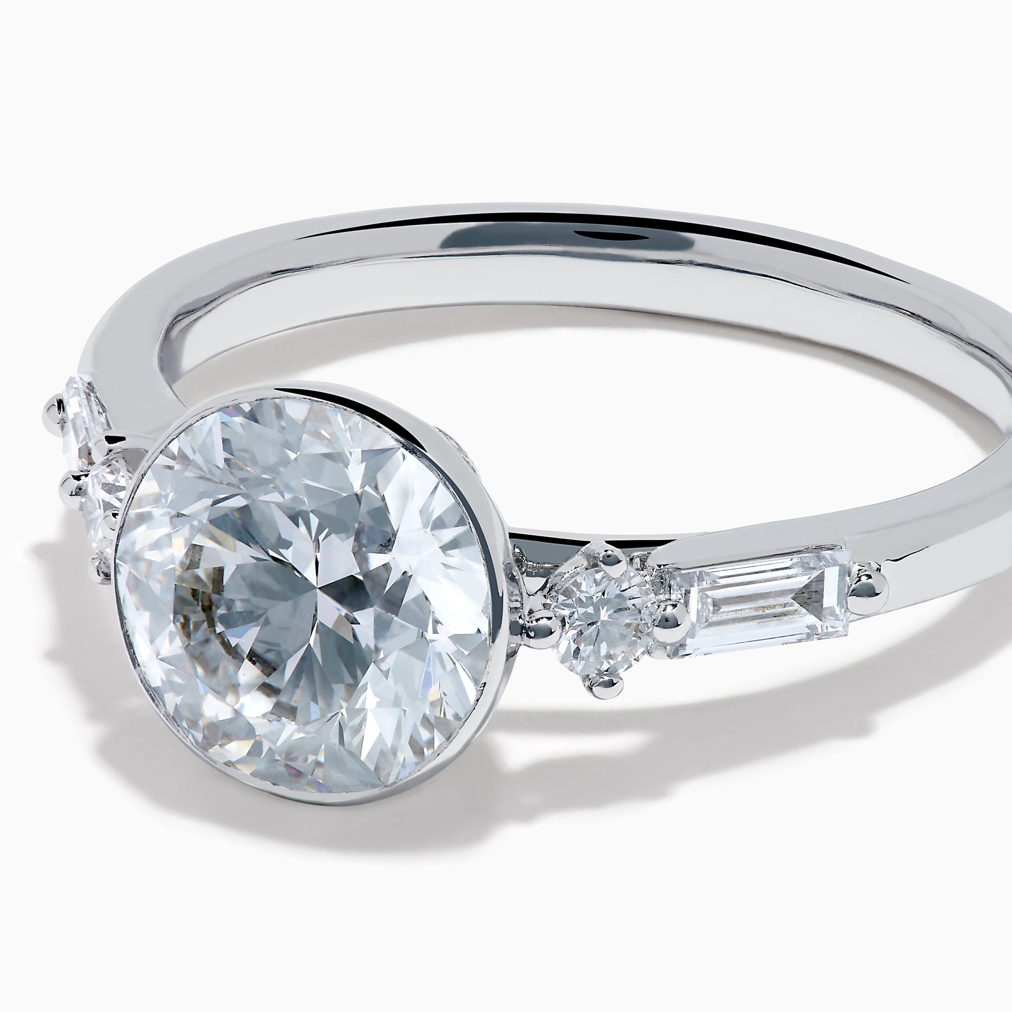 The Star Lab Grown Diamond Moderne Ring in 18K White Gold showcases a large round center diamond with two smaller diamonds on each side, set on a sleek, polished band against a white background.