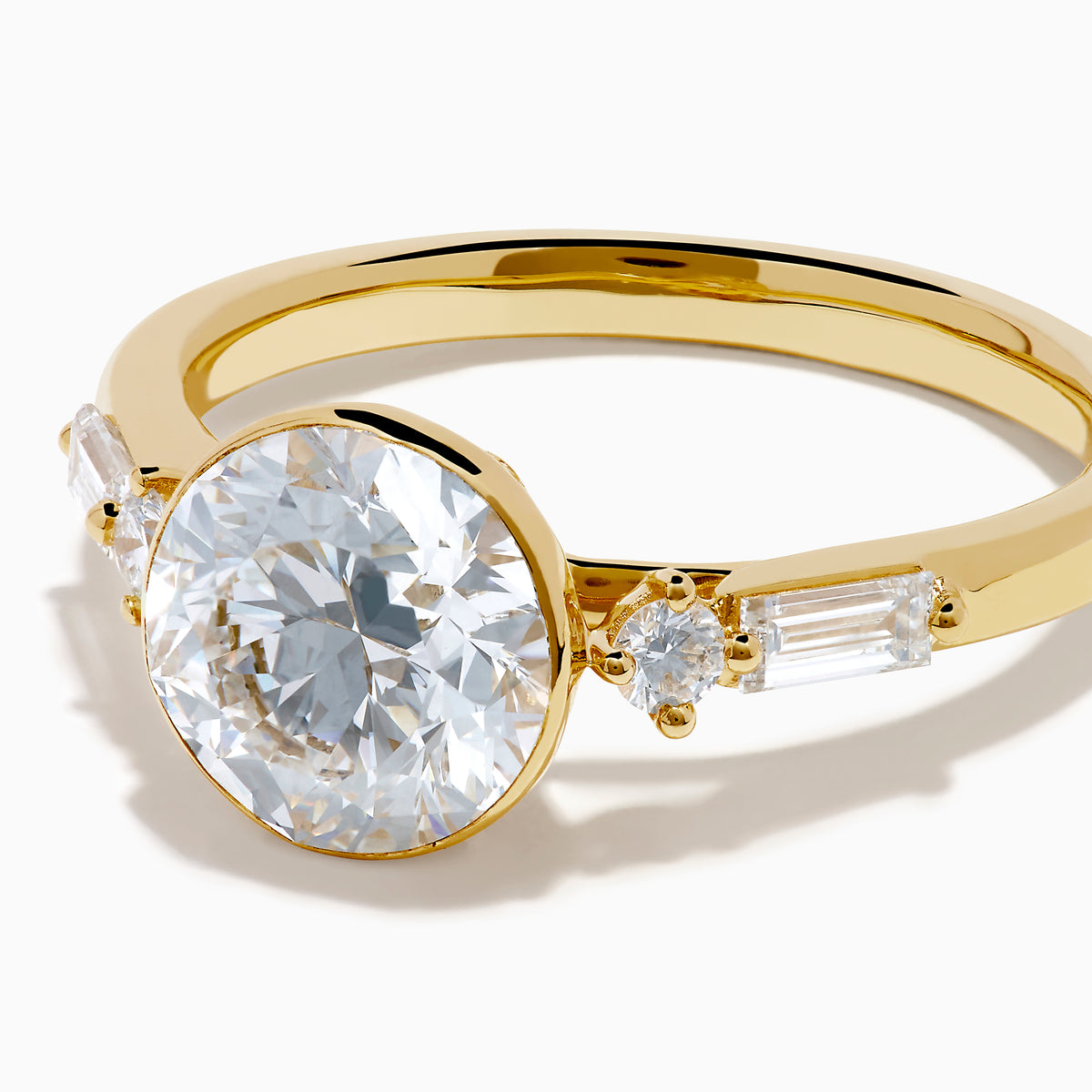 The Star Lab Grown Diamond Moderne Ring in 18K Yellow Gold features a large round lab diamond center, two smaller round diamonds, and baguette-cut side diamonds, shown on a white background.